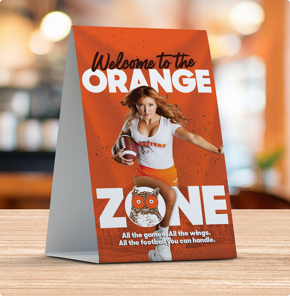 Table tent with text “Welcome to the ORANGE ZONE,” showing a Hooters girl holding a football.