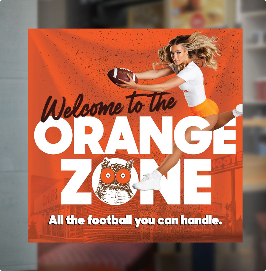 Window cling with text “Welcome to the ORANGE ZONE,” showing a Hooters girl holding a football.