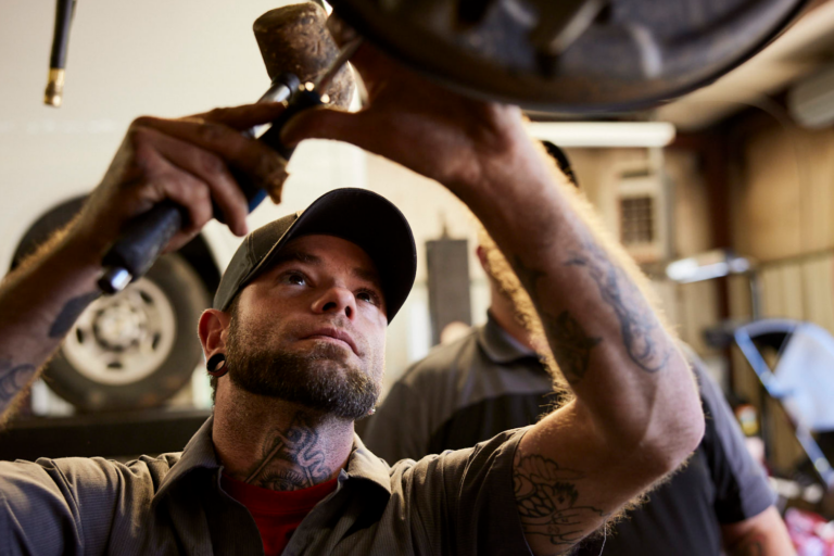 Mechanic wearing a cap, working on a vehicle part under a shop light.