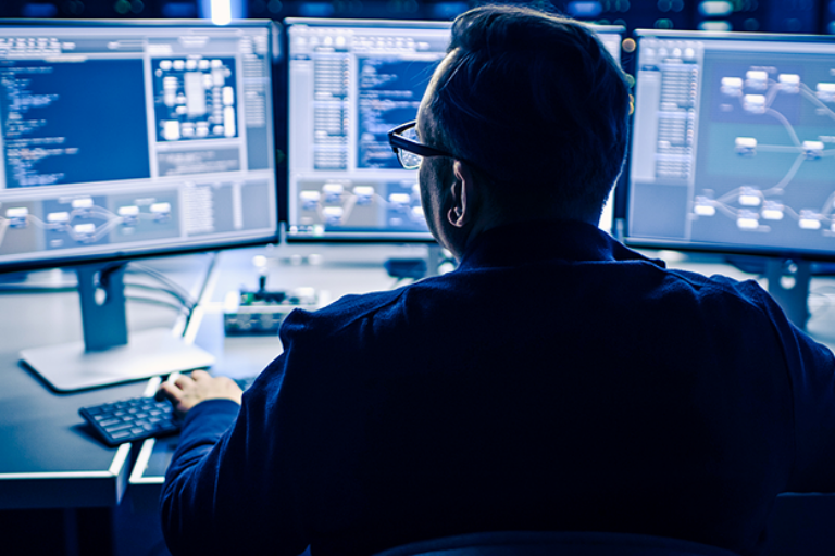 A man at a bank of monitors working on data